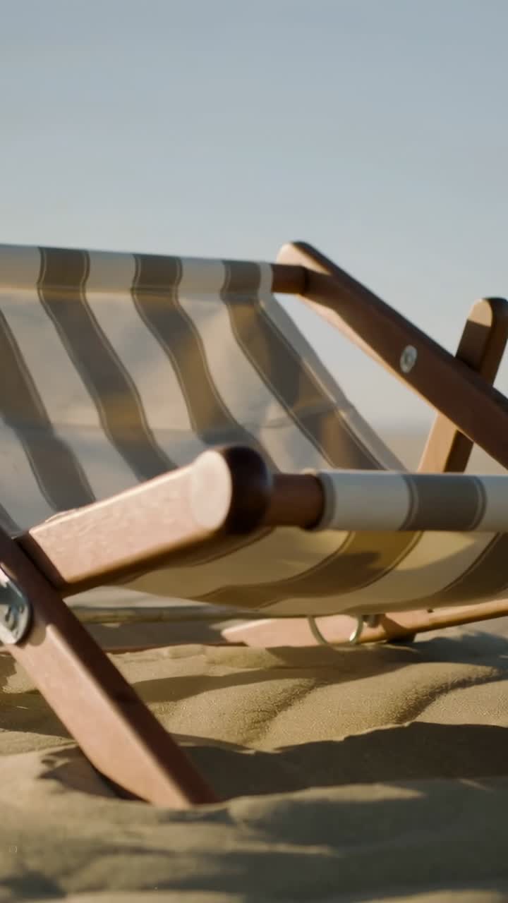 Chaise de plage rayée vide sur sable doré avec le vent soufflant