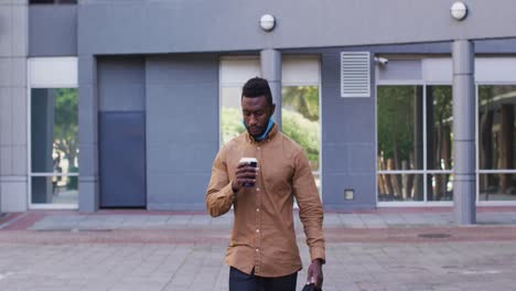 African-american-businessman-with-face-mask-drinking-coffee-in-street