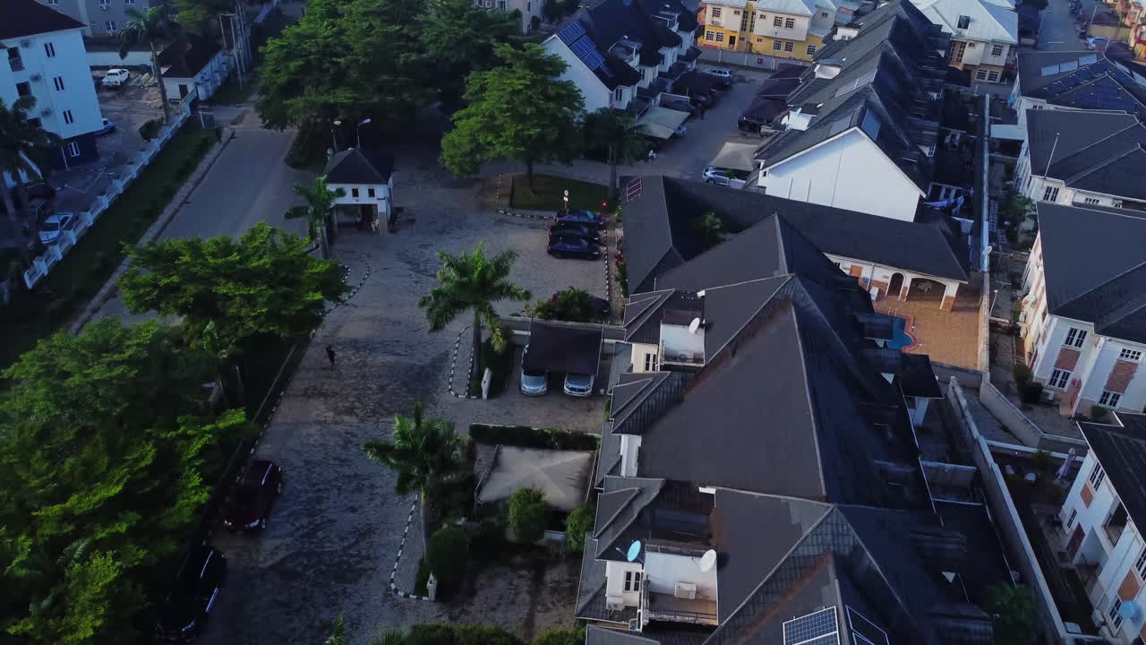 Beautiful aerial of photovoltaic solar panels on the rooftops of modern houses in a luxury neighborhood in Abuja, Nigeria. A man walk around the house towards the entrance gate