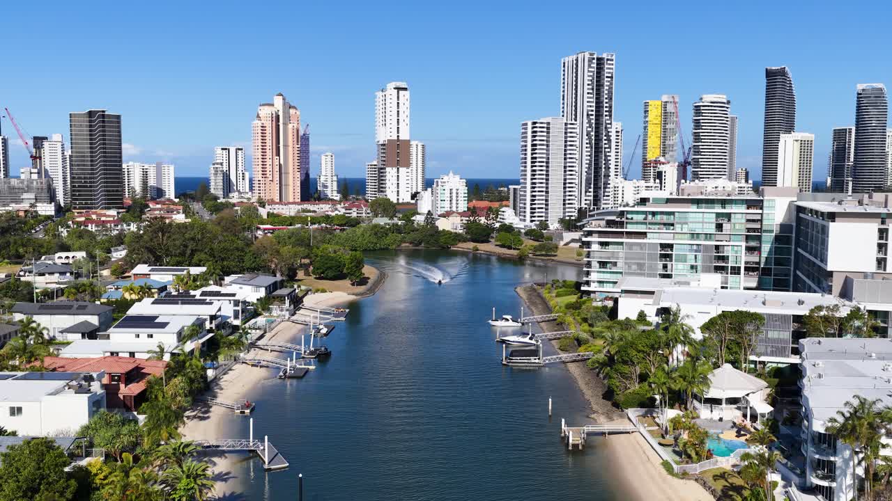 Drone flies over Gold Coast canal, tracking a boat with modern skyline and bright daylight