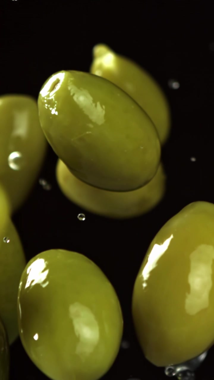 Olive verdi che cadono al rallentatore con gocce d'acqua su sfondo nero