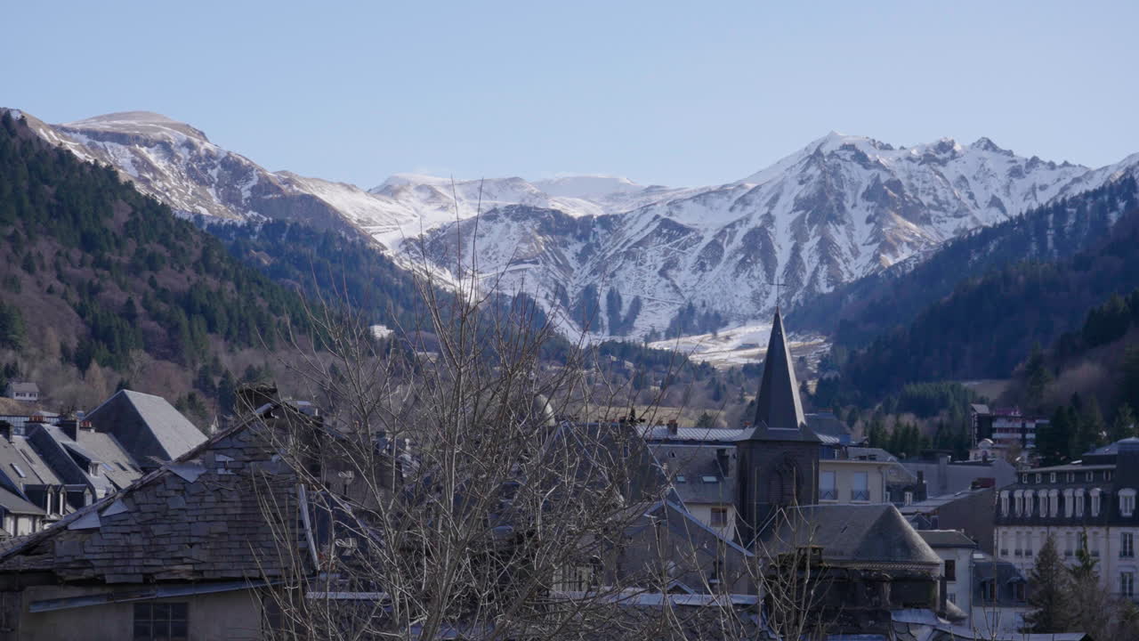 WIde shot of a small village in France, snowy mountains in the background in a sunny winter weather