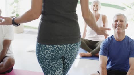 happy diverse seniors sitting on mats in pilates class with female coach, unaltered, in slow motion