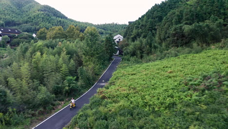 Toma-Aérea-De-Una-Persona-Conduciendo-Una-Moto-Por-Una-Carretera-Vacía-En-Un-Bosque-De-Bambú