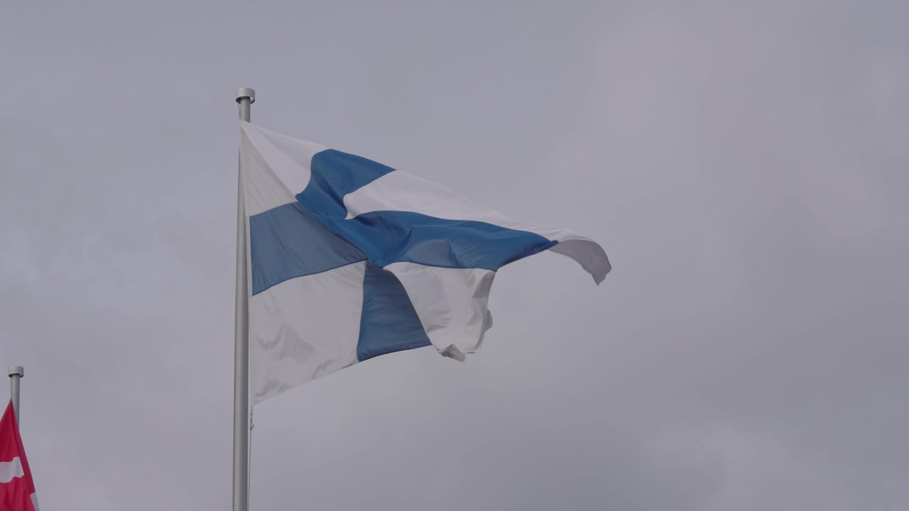 Finlands nationalflag på flagstang, der vajer i vinden mod en klar himmel. Lav vinkel, slowmotion.