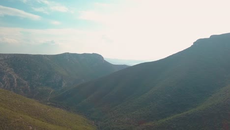 Dron-Disparó-Hacia-Adelante-Sobre-Un-Valle-Entre-Montañas-Y-En-El-Lejano,-El-Mar