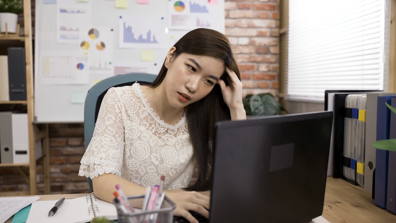 갑작스러운 심한 두통으로 고통받는 아시아 여성 매니저의 초상화는 밝은 오피스텔의 책상에서 노트북에서 일하는 동안 그녀의 사마귀를 문지르고 있습니다.