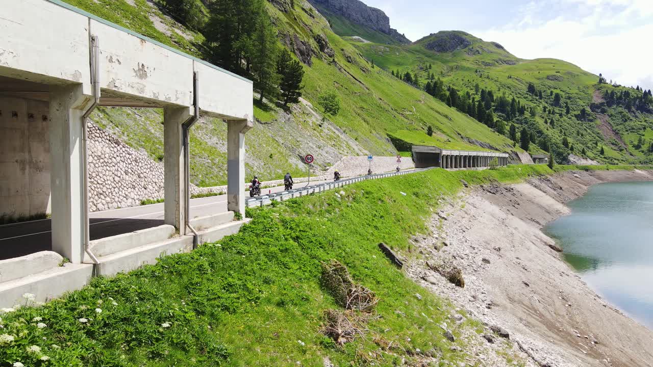 Curved alpine tunnel guides bikers through Dolomite pass near emerald lake, 4K