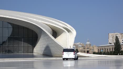 white minibus drives directly in front of the imposing and futuristic heydar aliyev center in baku