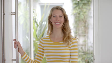 Portrait-of-happy-caucasian-woman-with-blonde-hair-smiling-in-doorway-at-home,-slow-motion