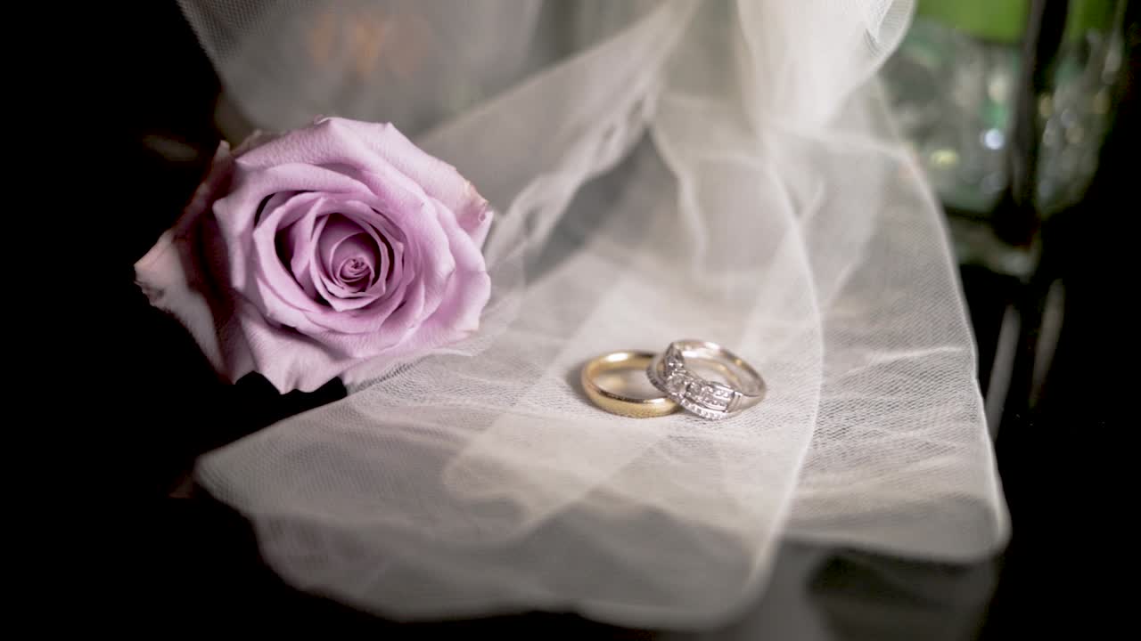Wedding rings on sheer fabric with lavender coloured rose flower