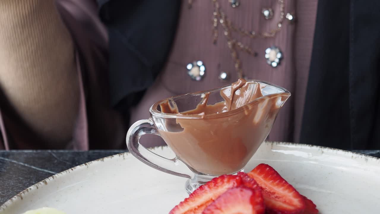 여자 는 초콜릿 폰듀 에 딸기 를 담그고 있다