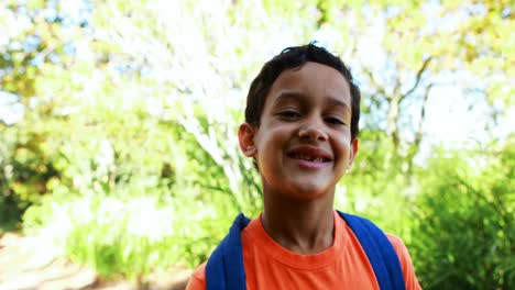 portrait of cute boy with schoolbag standing in park