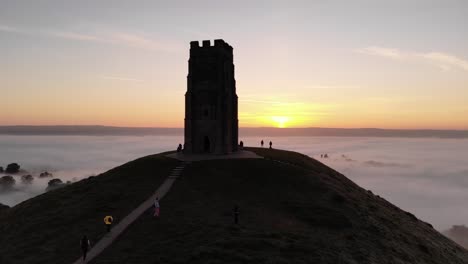 people climbing up the misty glastonbury tor at sunrise in somerset