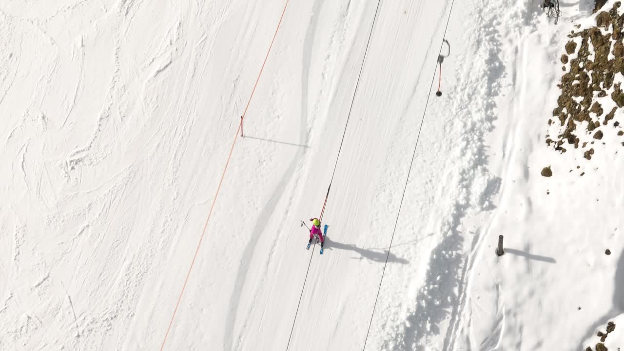 Idyllic overhead drone shot of a skier climbing to the top of a mountain slope being pulled by a ski lift during winter vacation