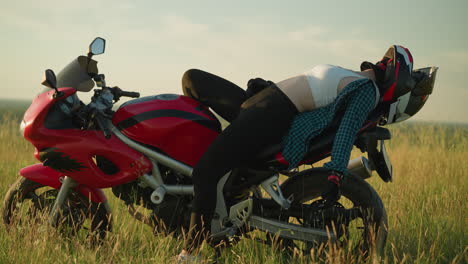 a young woman is lying back on a red power bike in an open grassy field under the sun, she wears a helmet and gloves, relaxing in the serene countryside