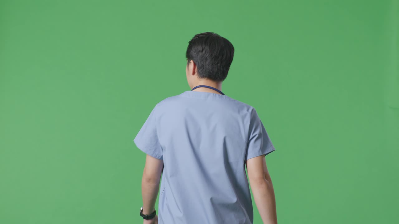 스테토스코프를 들고 있는 아시아 남성 의사가 병원 안의 녹색 스크린 배경에서 돌아다니고 있는 모습