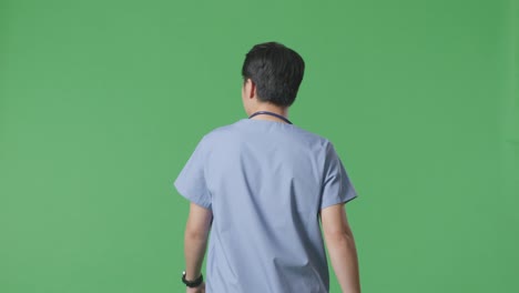 back view of asian male doctor with stethoscope looking around and walking on green screen background in the hospital