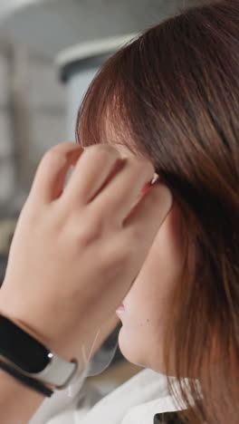 색 코트를 입은 학생이 보호 얼굴 방패를 들고, 그것을 입고, 좌석에서 휴식을 취하고, 왼손에 스마트 시계와 검은 팔를 가지고, 워크에서 형광 조명 아래