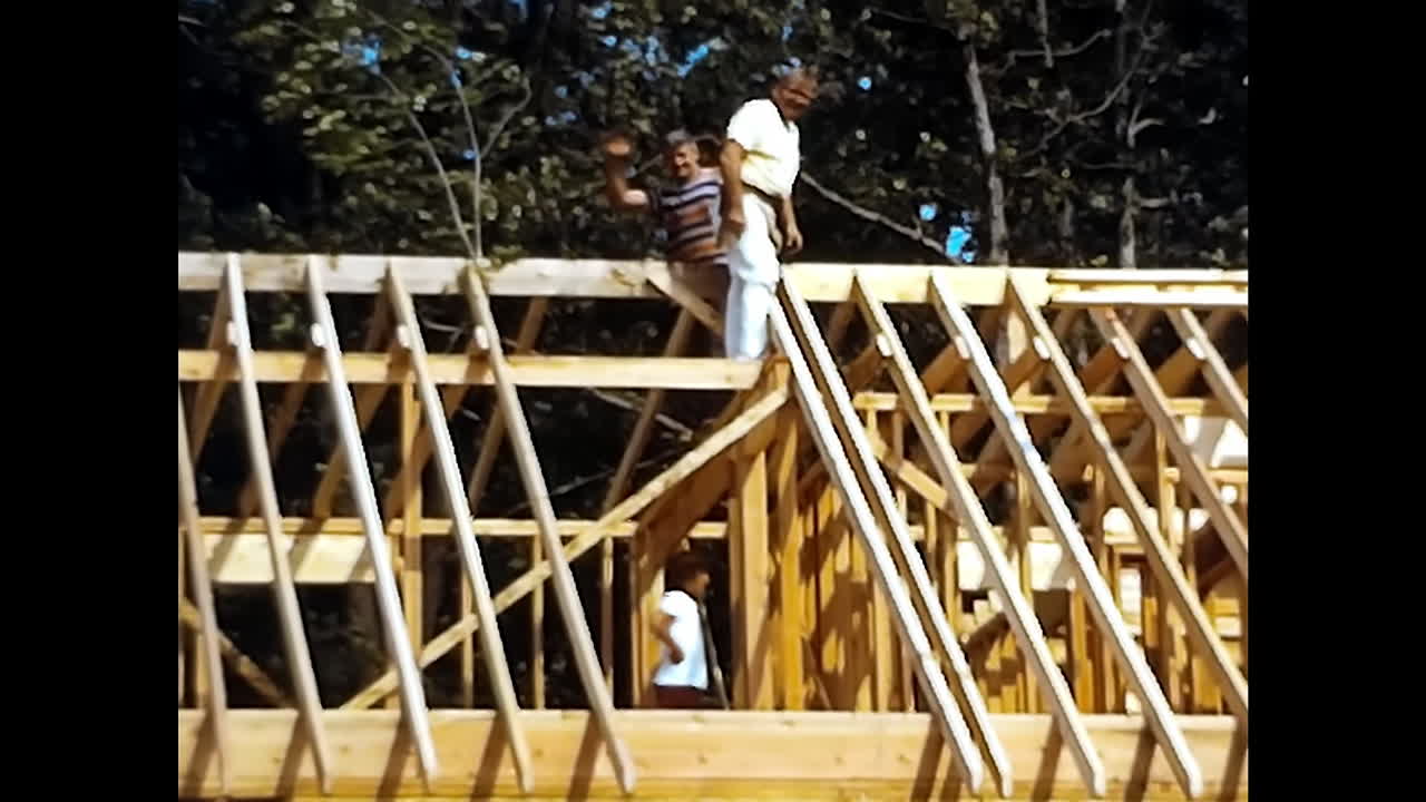 Man Standing on Wooden Roof in 1970s USA. CIRCA USA - 1970s: A man is seen standing on top of a wooden roof in the USA during the 1970s.