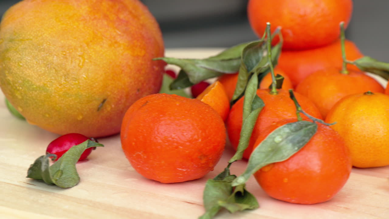 Composition with sliced oranges, mango, rosehip and green leaves, close up with water drops