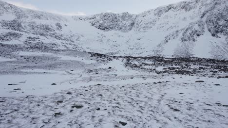 Aerial-drone-footage-panning-around-the-headwall-of-Coire-an-t-Sneachda-in-the-Cairngorm-mountains-of-Scotland-in-snow,-ice-and-full-winter-mountaineering-conditions-to-reveal-gullies-and-couloirs