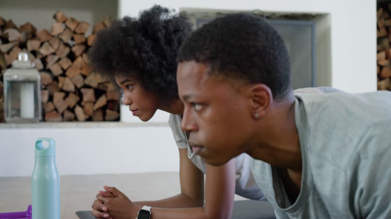 African descent couple starting plank on mats at home in gymwear, glancing watch, resting for core