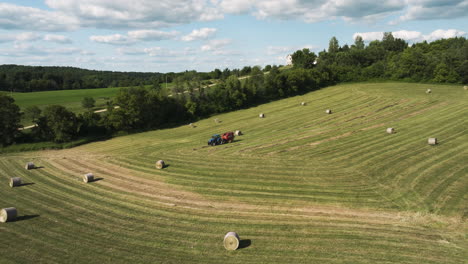 round hay bales in the farm with hay baler in the distance