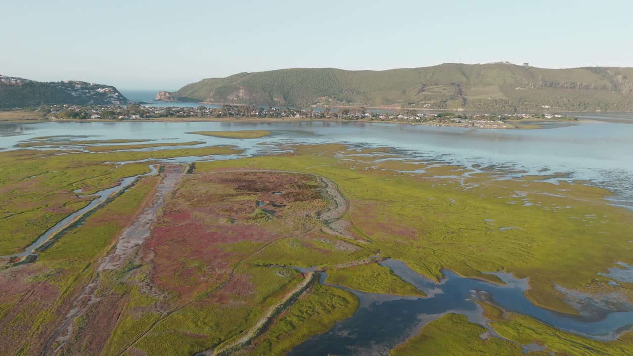 Ripresa aerea con drone che inizia sopra l'estuario di Knysna e si inclina in avanti per rivelare le Knysna Heads in lontananza, con ampie vedute costiere, luce naturale e un drammatico paesaggio sudafricano.