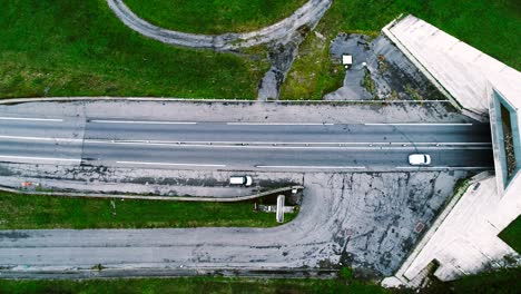 aerial view with a drone over highway roads going into a tunnel in france. only grass fields and trees around the roads. cars and trucks driving on the roads.