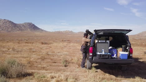 Young-Man-Searches-for-Falconry-Equipment-in-Black-Truck-Parked-in-Desert