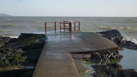 Concrete-platform-on-Portmarnock-Beach,-Ireland,-with-waves-crashing-in-the-background