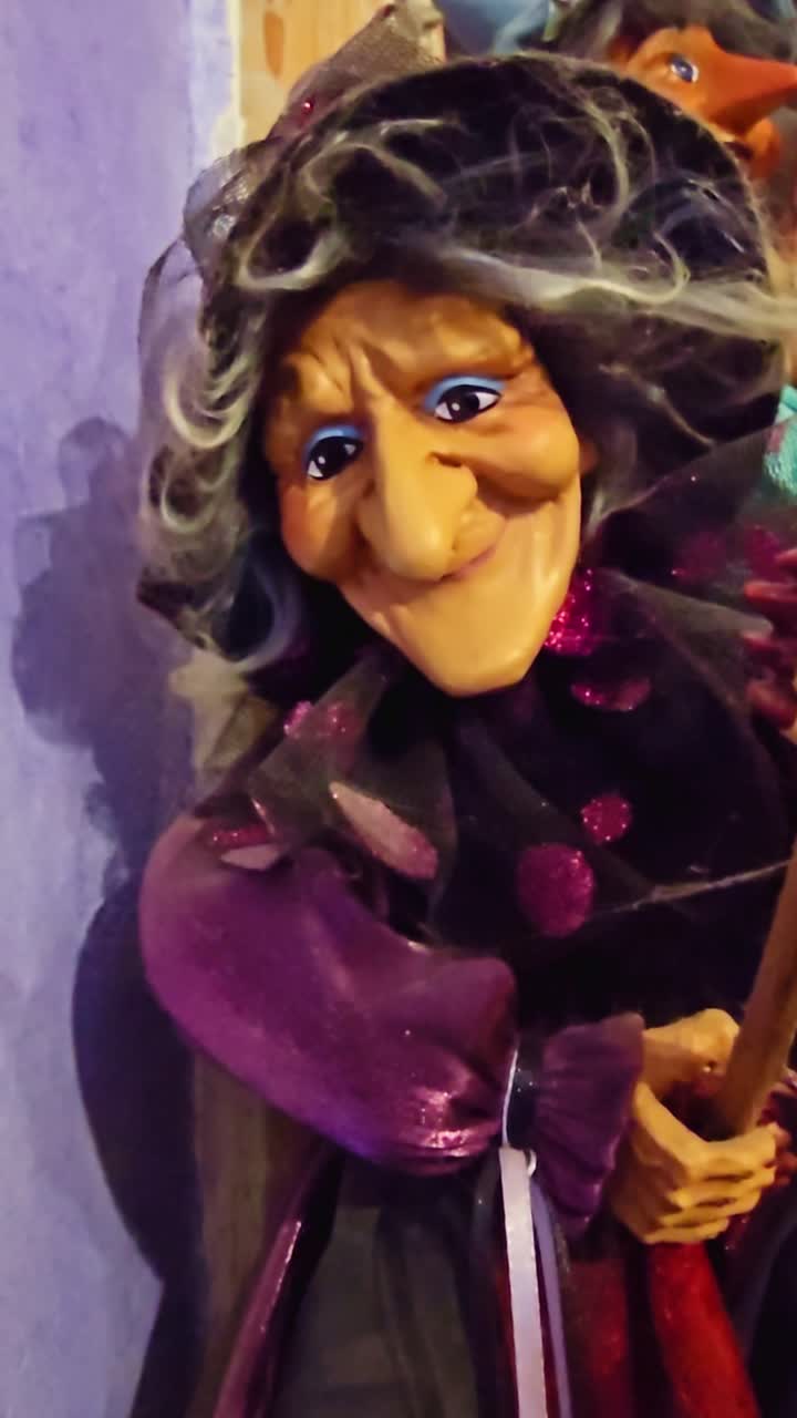 A vertical shot of a witch doll with a long nose, wrinkled face, and colorful clothing, captured indoors with warm lighting