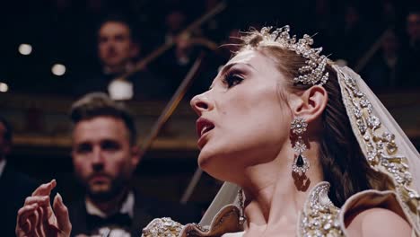 talented opera singer performing a beautiful piece on a stage, wearing an elegant dress and jewelry, with the orchestra conductor directing the musicians in the background