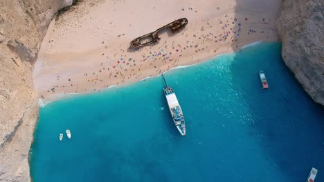 turistas que visitan un barco naufragado en la playa de arena aislada por acantilados blancos