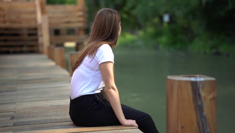 young caucasian girl sitting on side of wooden bridge looking into distance