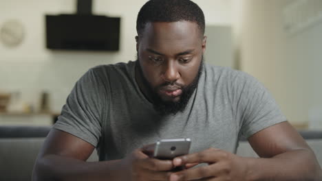 concentrated man sitting with phone. portrait of black man typing message.