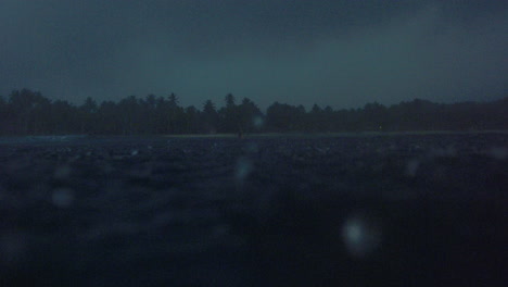 rain droplets bounce across ocean water surface with tropical forest coastline