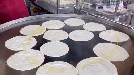 experto en panadería haciendo parathas y aceitándolas en una gran sartén - comida callejera de pakistán