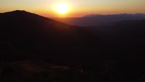 A-drone-rises-up-into-the-sky-at-sunset-in-the-silhouettted-mountains-near-Estepona,-Spain