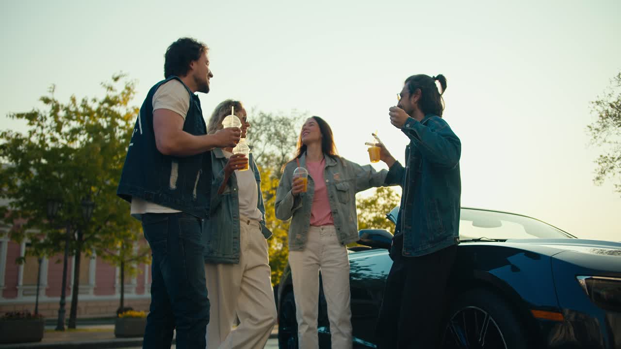 손에 테일을 들고 있는 젊은이들이 은 날에 값비싼 차 근처의 거리에서 소통합니다.