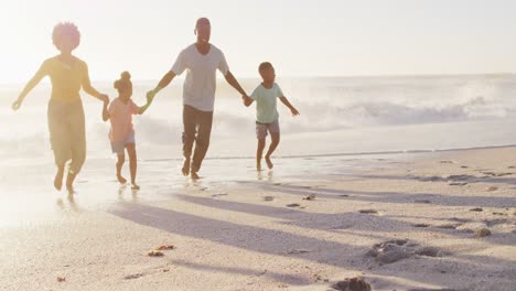 smiling african american family walking and holding hands on sunny beach