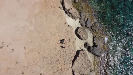 people standing on the edge of a cliff next to the sea, drone 4k