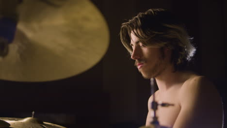 young shirtless male drummer with beard playing drums