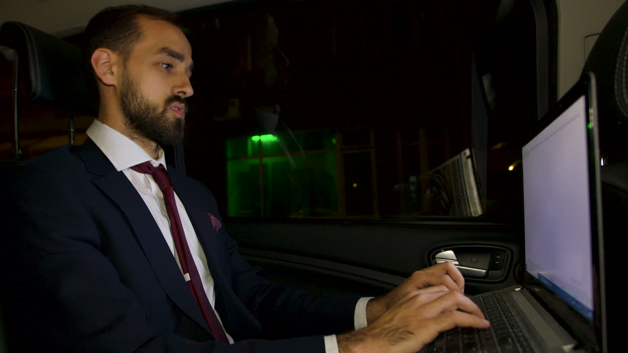 hombre de negocios en traje sentado en el asiento trasero de su limusina trabajando en una computadora portátil