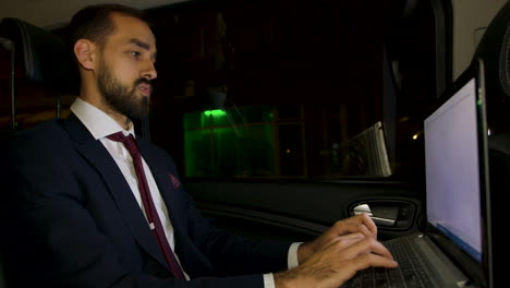 businessman in suit sitting on the back seat of his limousine working on laptop