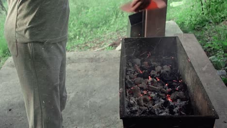 young man blows coals in brazier