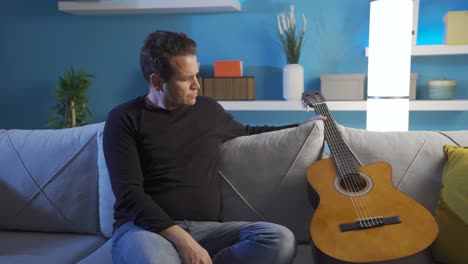 sad and unhappy man playing his guitar at home. distressed and sad guitarist.