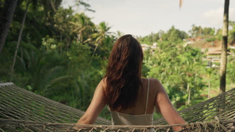 una morena con el cabello suelto se balancea suavemente en una hamaca con vistas a las exuberantes terrazas de arroz