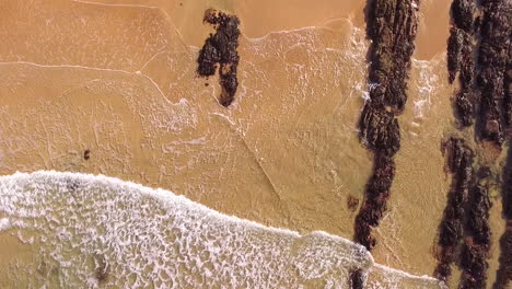 Luftaufnahme-Mit-Direktem-Blick-Auf-Die-Wellen,-Die-Sich-An-Einem-Sandstrand-Mit-Einigen-Felsen-An-Der-Küste-Von-Gower-In-Wales-Im-Vereinigten-Königreich-Brechen